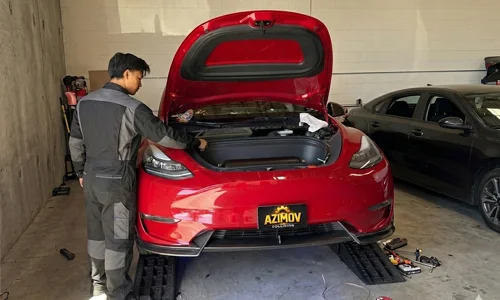 Mechanic performing battery repair in the trunk of a red Tesla at Azimov Collision service center in California