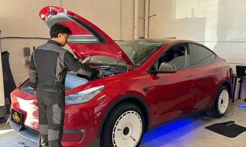 Mechanic performing repair in the front trunk (frunk) of a red Tesla Model Y at Azimov Collision service center